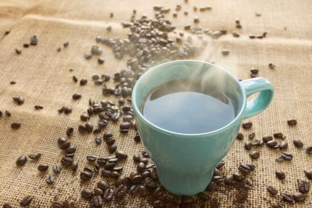 Tasse de café à grains chaude, avec fèves de café autour